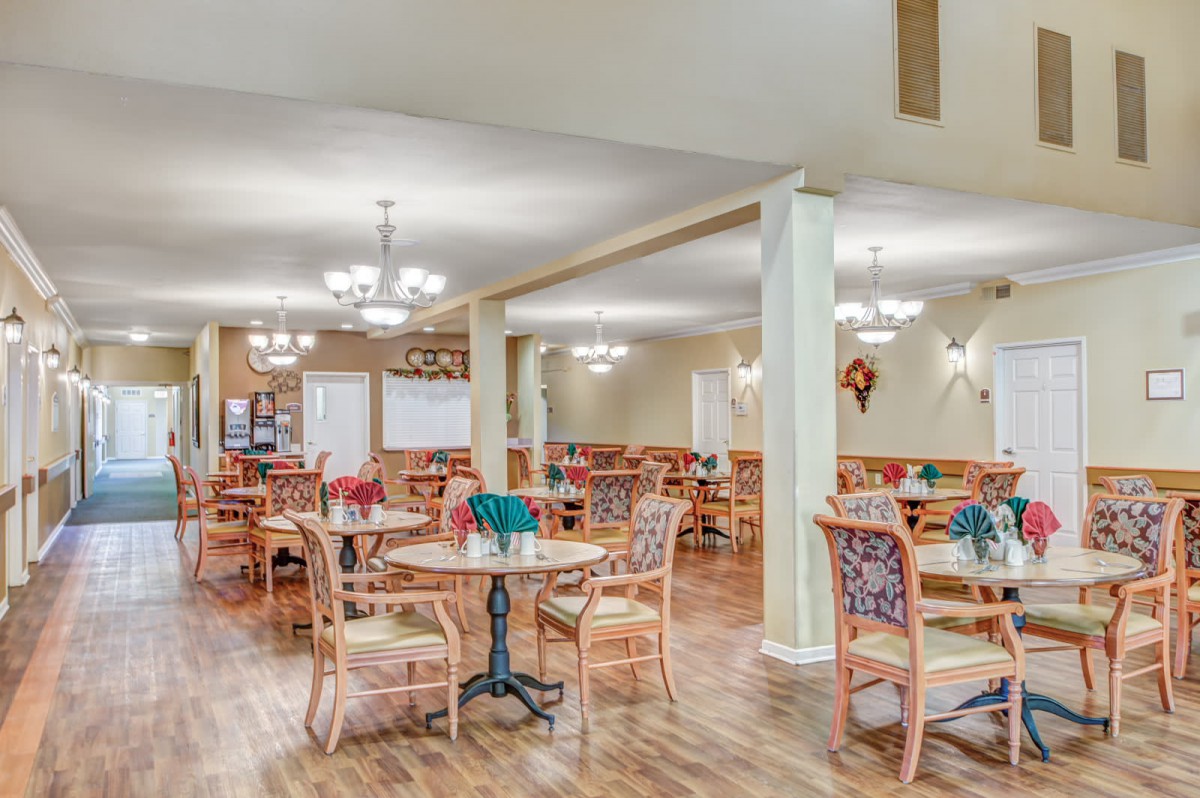 A spacious dining area with neatly arranged tables and chairs, illuminated by elegant chandeliers.