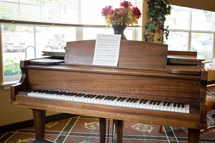 A grand piano with sheet music and a vase of flowers on top, set in a sunlit room.