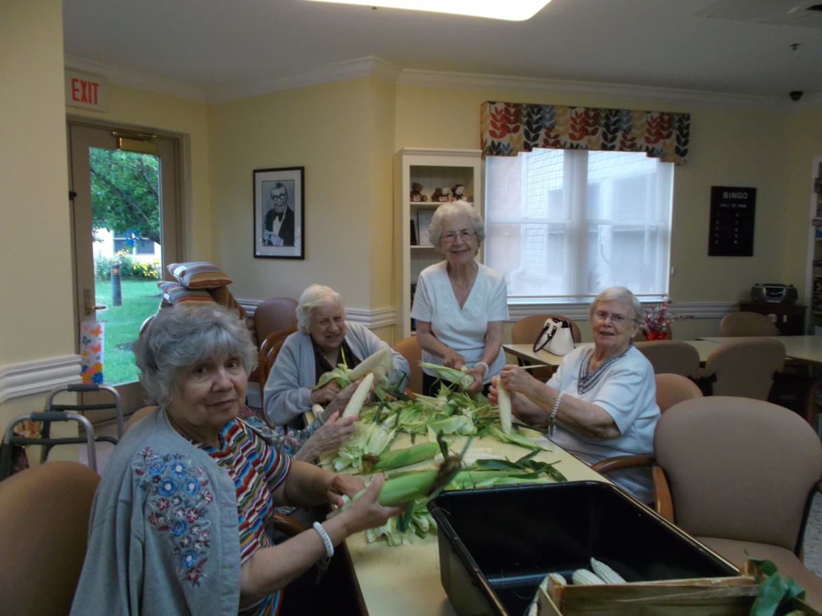 A group of elderly individuals preparing corn together indoors.