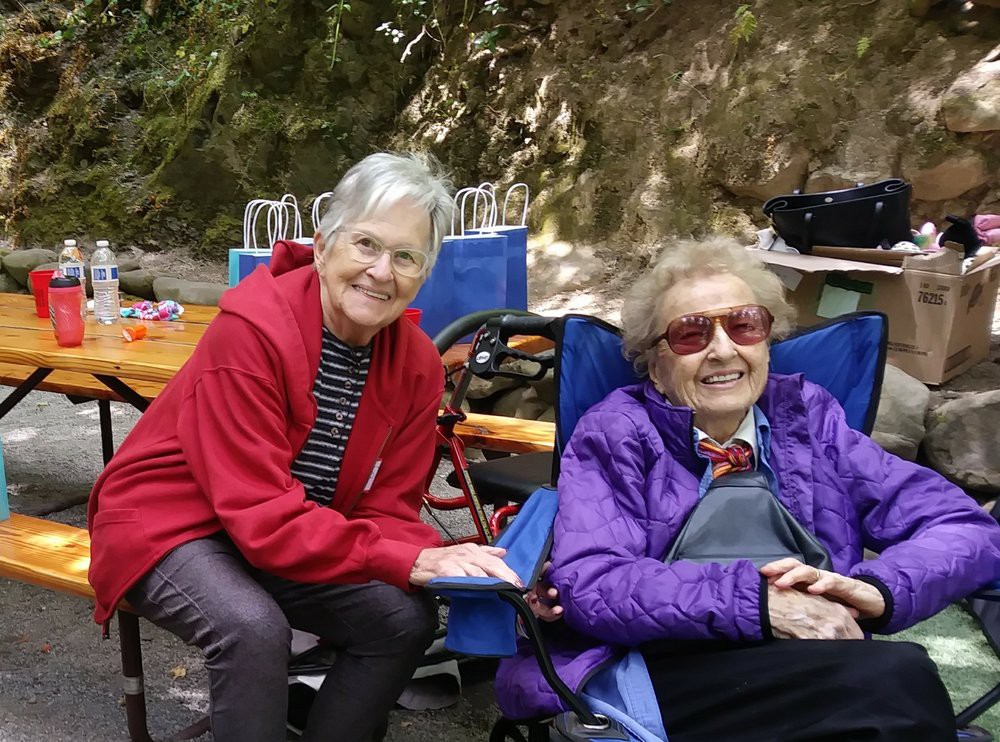Two elderly women enjoying a sunny day outdoors, sitting comfortably in chairs.