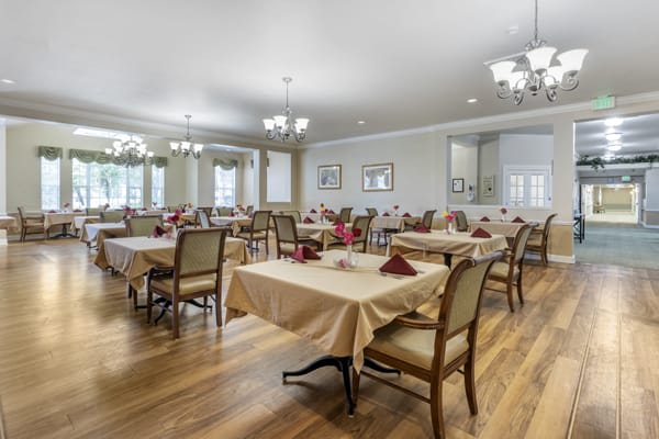 An elegant dining room with neatly arranged tables and chairs, featuring chandeliers and wooden flooring.