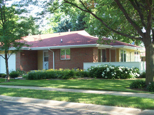 A charming brick house surrounded by lush greenery in a suburban neighborhood.