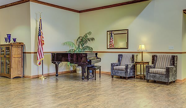 A room with a grand piano, American flag, armchair, lamp, mirror, and plant.