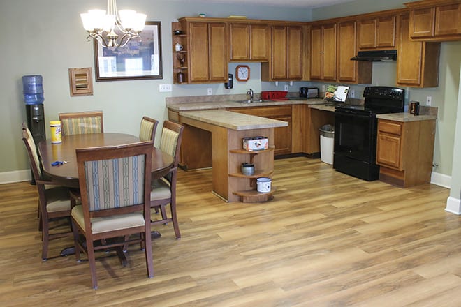 A modern kitchen and dining area featuring wooden cabinets, a hardwood floor, and a chandelier above the table.