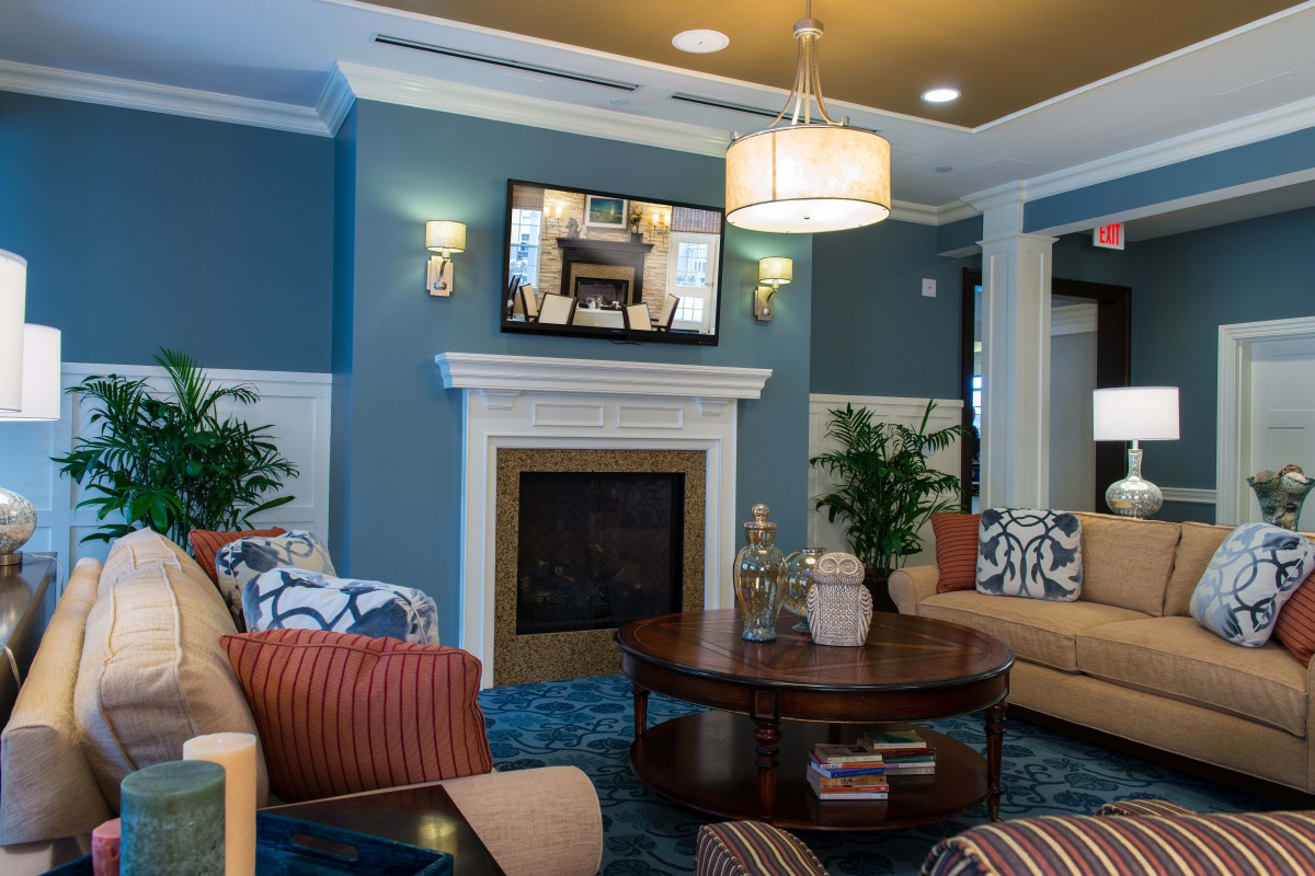 A cozy modern living room with blue walls, featuring a fireplace and a mounted television above it, surrounded by comfortable sofas and a central coffee table.