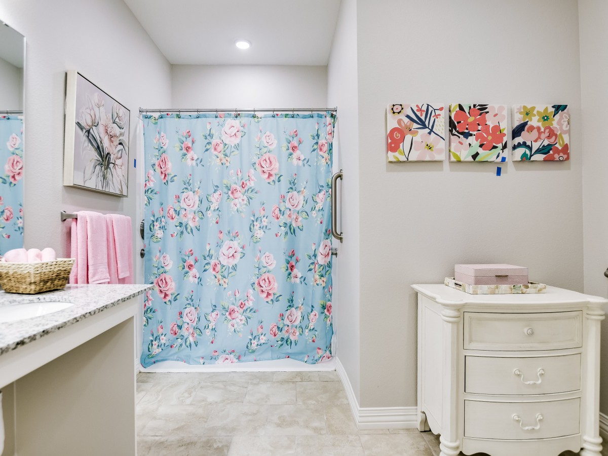 A well-decorated bathroom featuring a floral shower curtain, neatly arranged towels, and artwork on the walls.
