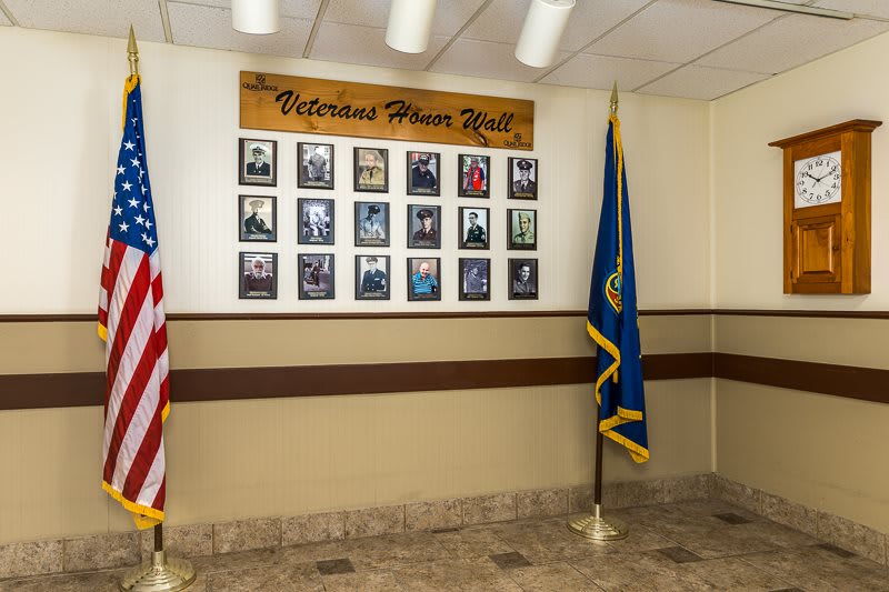A wall displaying a collection of photographs honoring veterans, accompanied by American and state flags.