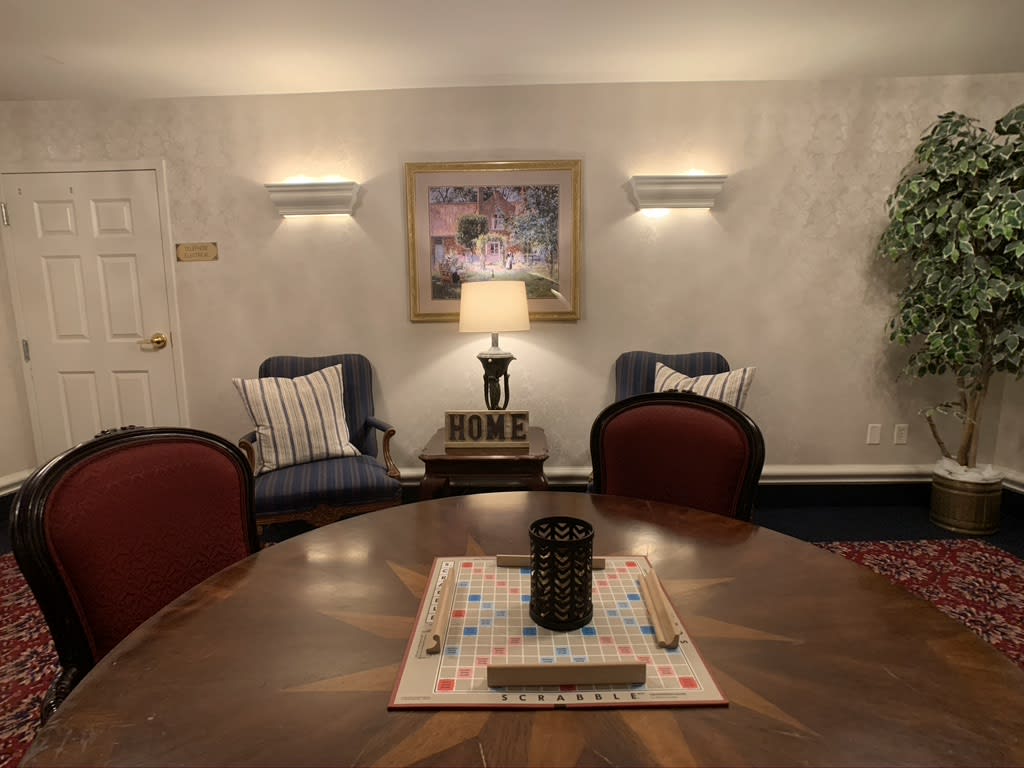 A cozy living room setting with a central table, surrounded by chairs and warmly lit lamps.