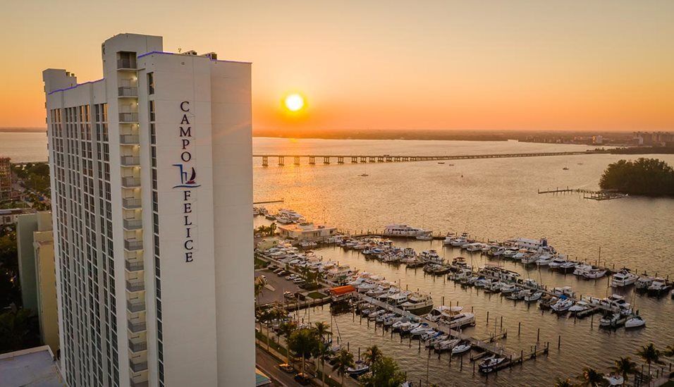 Sunset view over a marina with boats docked and a tall building nearby.