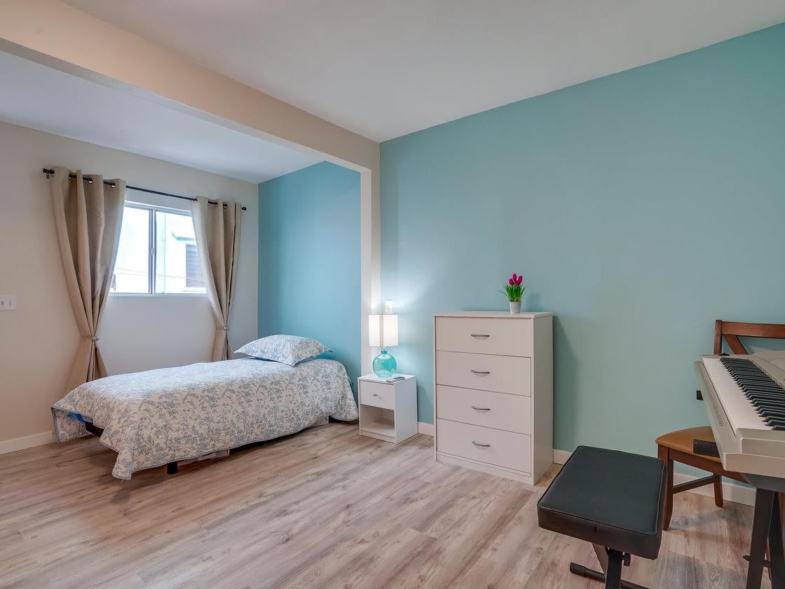 A cozy bedroom with a single bed, blue accent wall, and modern furnishings.