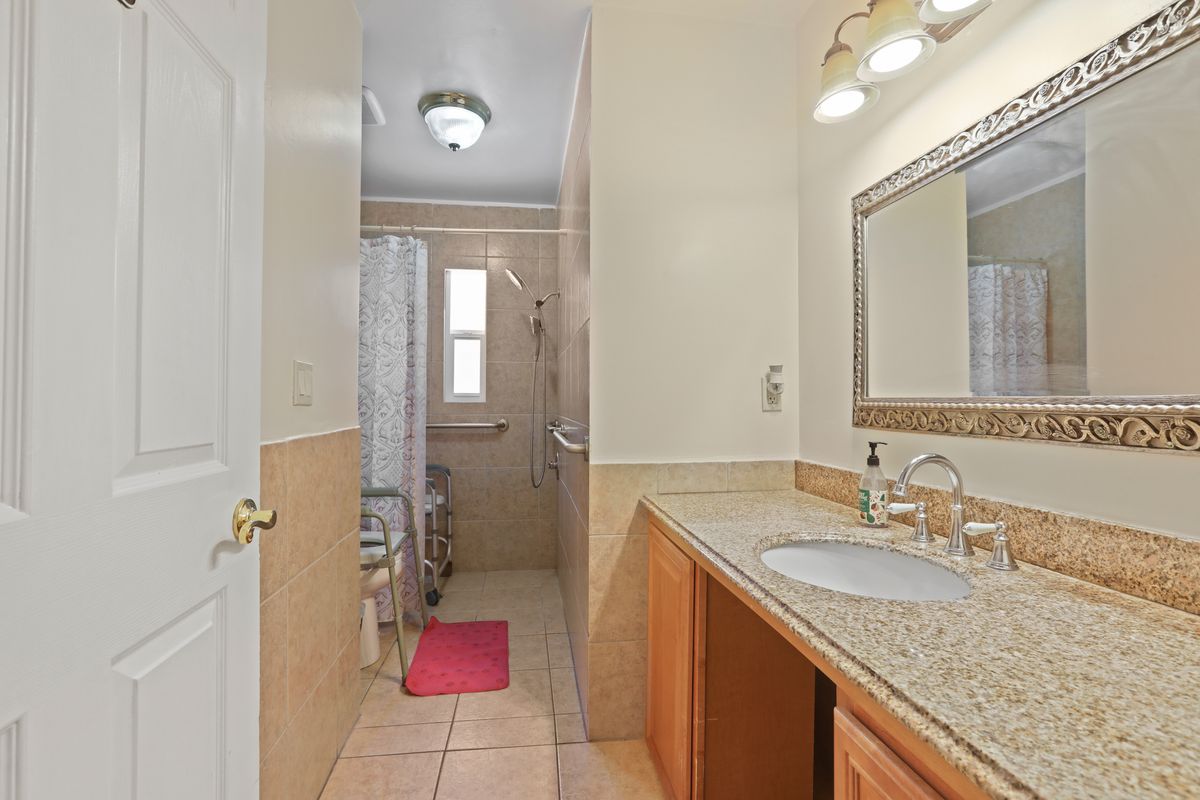 A spacious bathroom with a granite vanity, large mirror, and a tiled shower area.