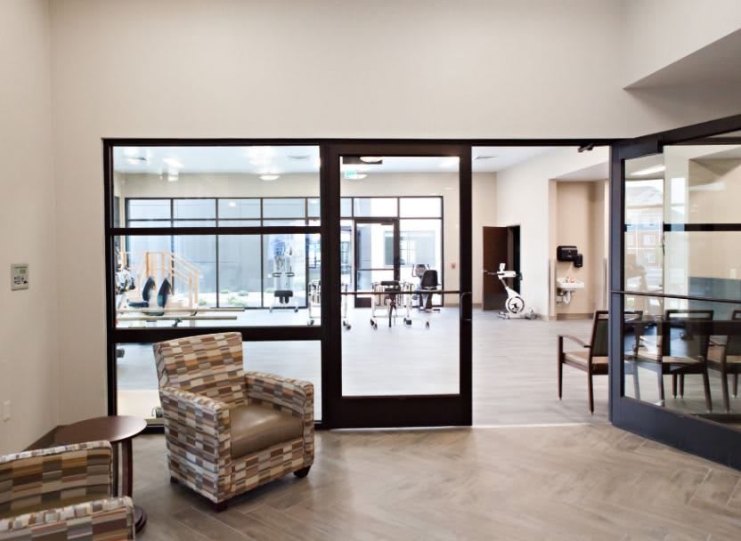 A modern office interior featuring a waiting area with patterned chairs and glass doors leading to an open workspace.