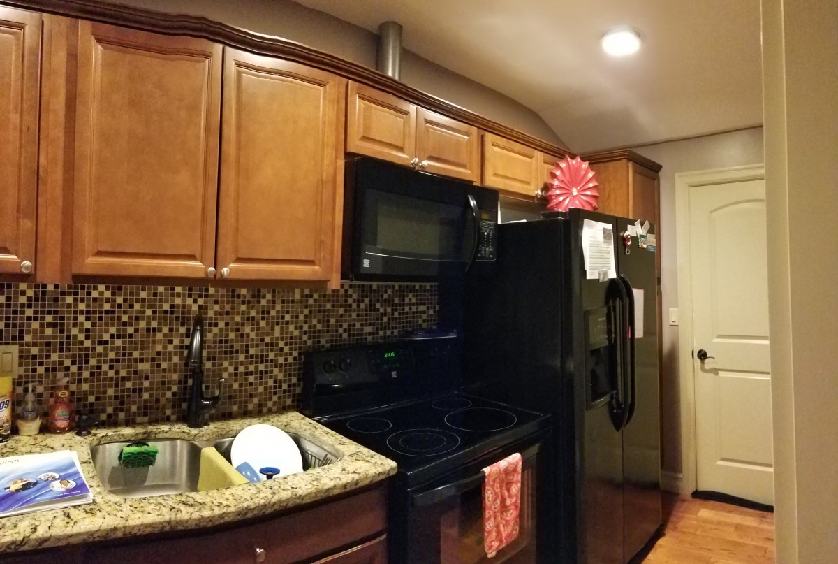 A cozy kitchen with wooden cabinets, a black refrigerator and microwave, and dishes drying on the countertop.