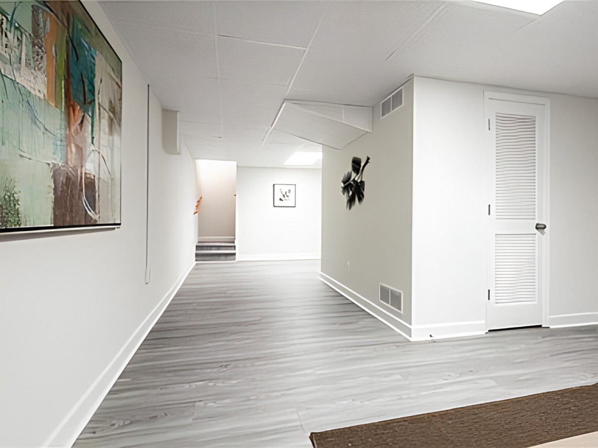 A modern, minimalist basement hallway with white walls and wood flooring.