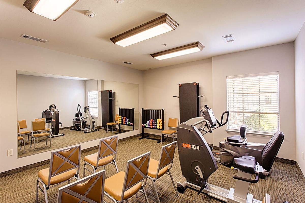 A small gym room with exercise equipment and chairs arranged in front of a mirror.