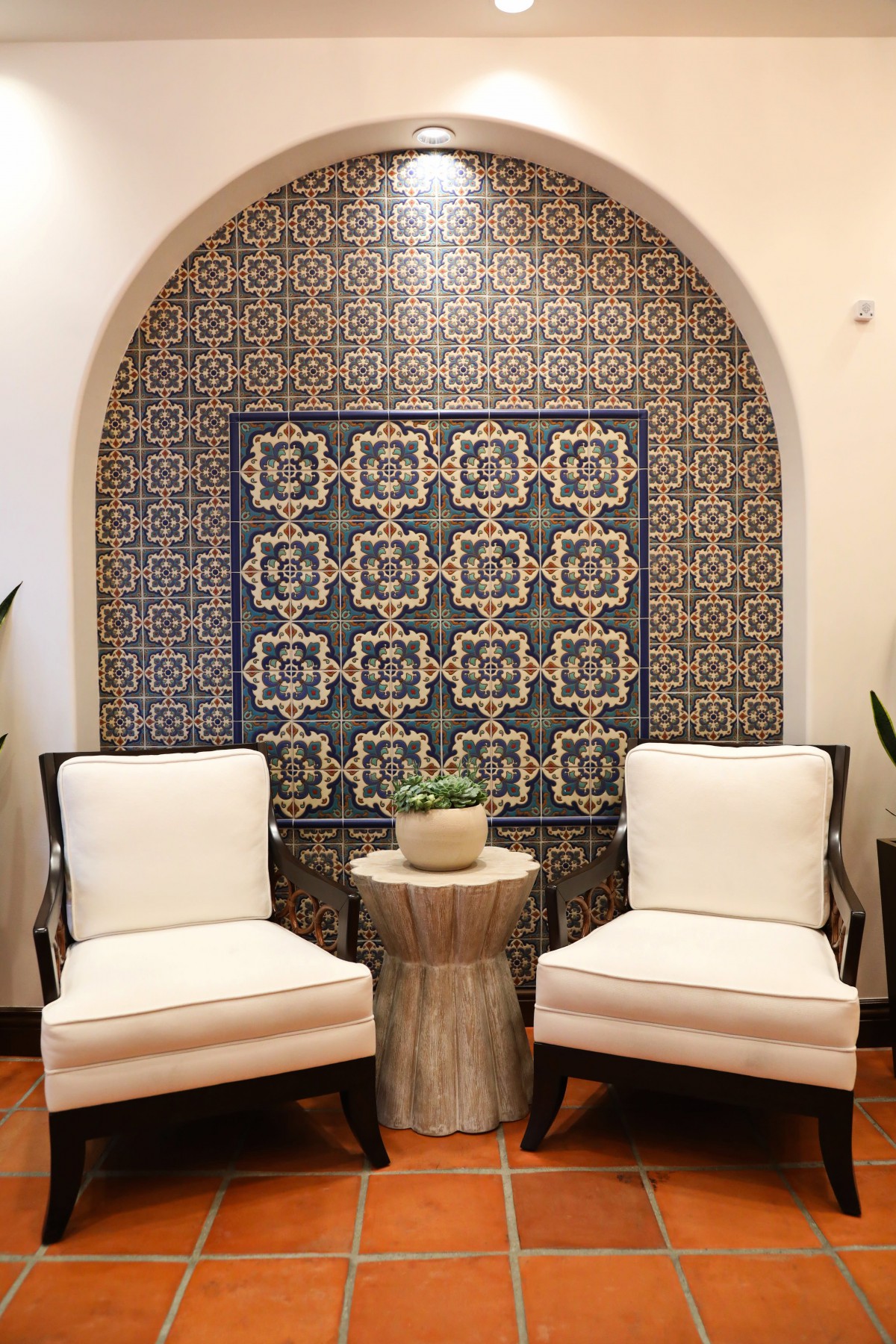 A cozy seating area featuring two comfortable chairs, a small side table with a plant, and an intricately designed mosaic tile wall.
