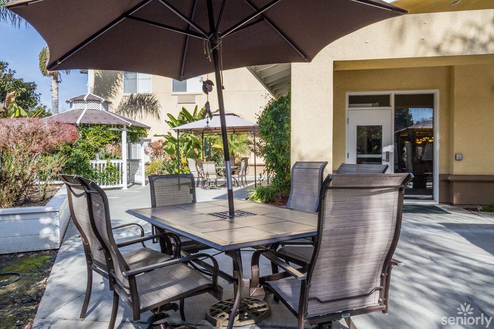 An outdoor patio setup with a table, chairs, and an umbrella in a garden setting.