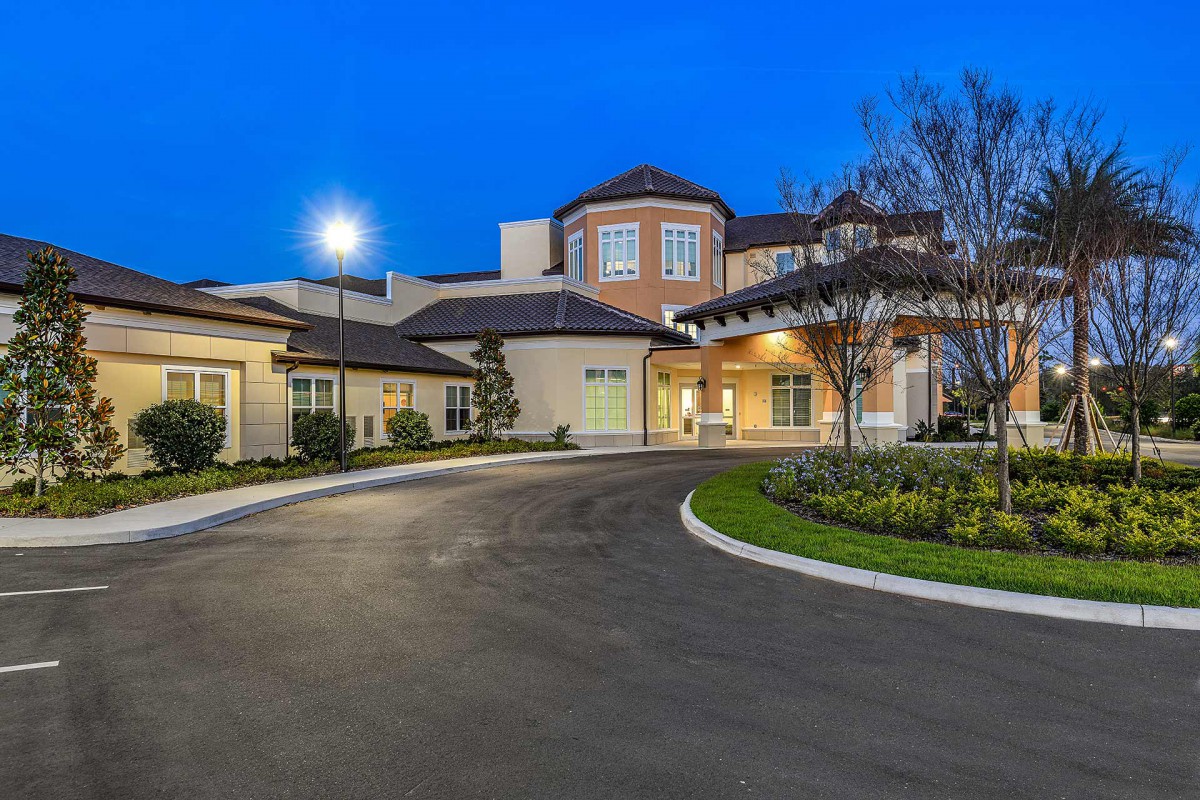 A luxurious mansion with a spacious driveway, beautifully lit at nighttime.