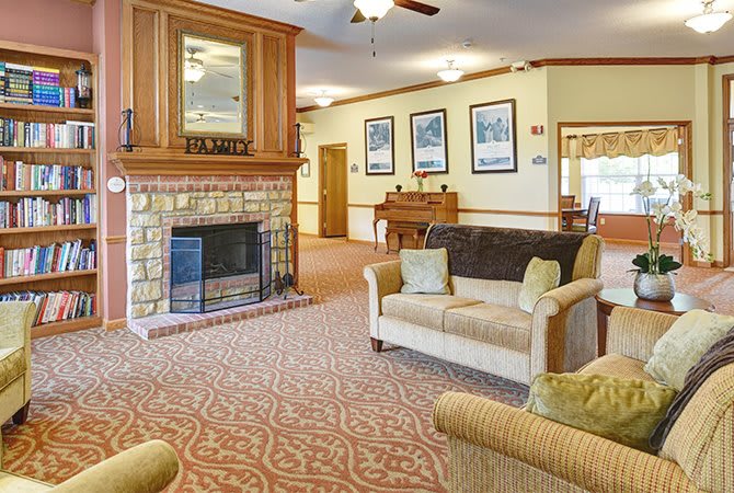 A cozy living room with a fireplace, comfortable seating, and a piano in the background.