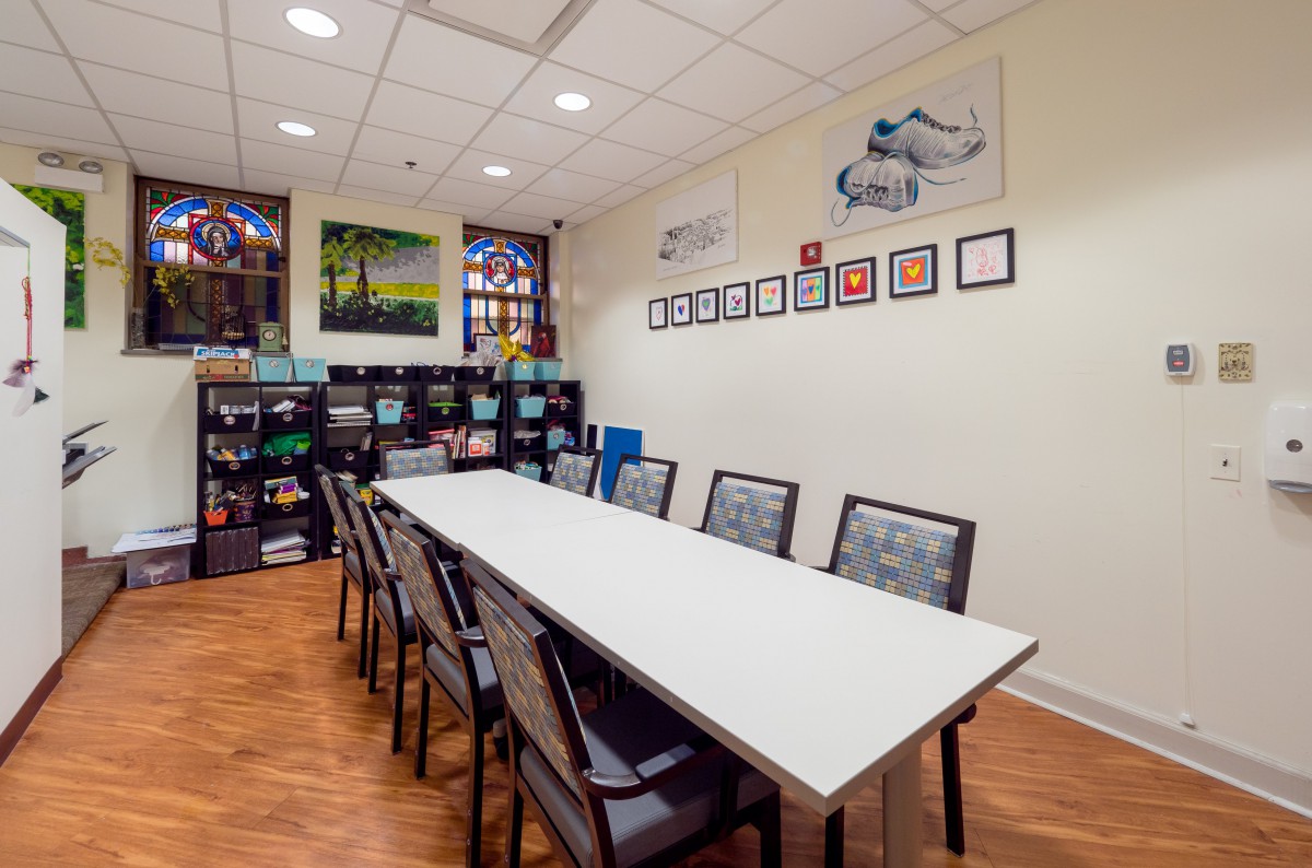 A well-organized meeting room with a long conference table, surrounded by chairs, bookshelves, and colorful artwork on the walls.