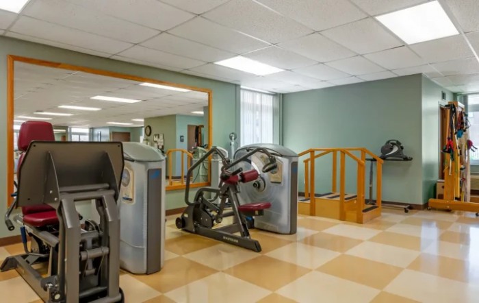 A gym room equipped with various fitness machines and a large mirror.