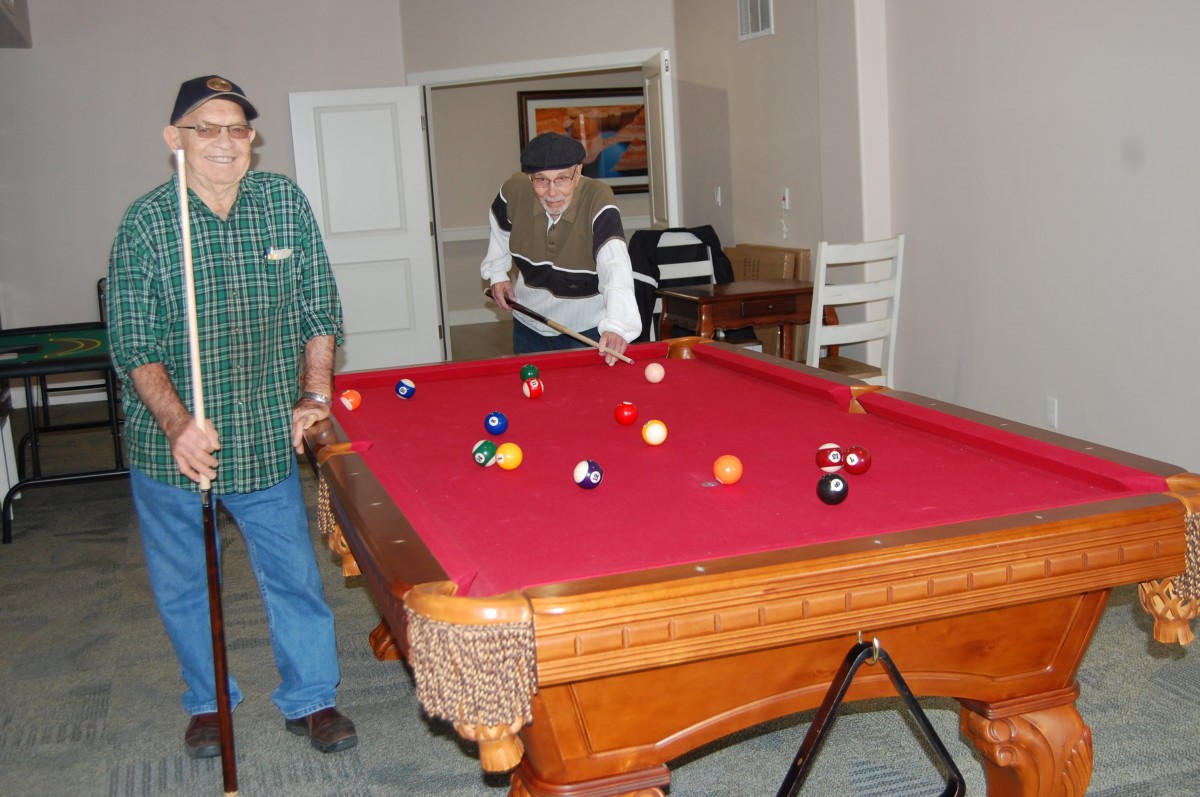 Two people engaged in a game of pool on a red pool table in a recreational setting.