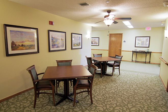 A cozy dining area with tables and chairs, featuring artwork on the walls and a ceiling fan.