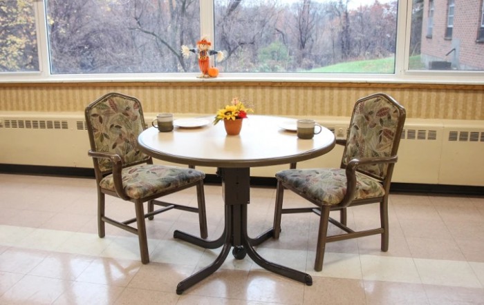 A small dining table with two chairs, adorned with a flower pot, positioned near a large window offering an outdoor view.