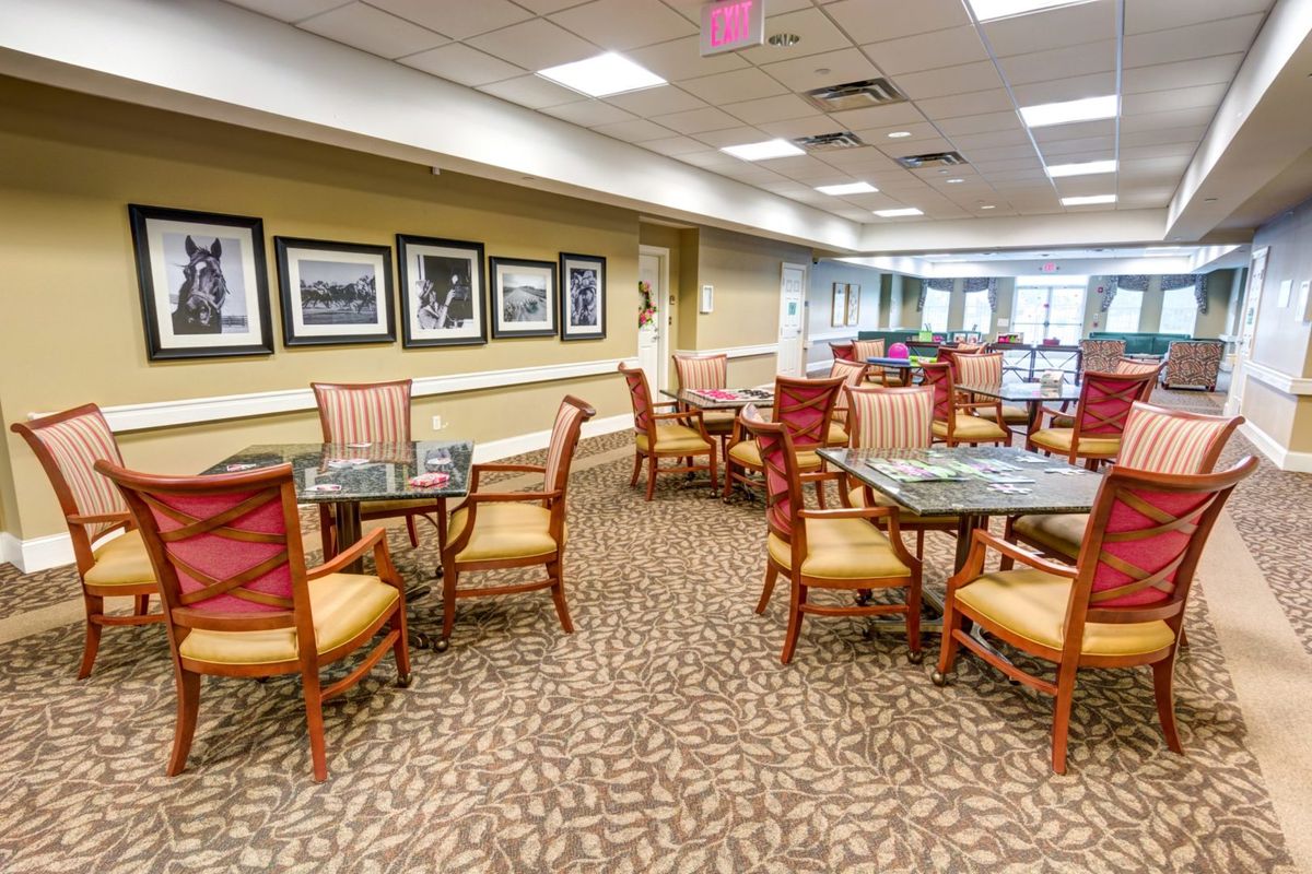 A spacious dining area with neatly arranged tables and chairs, carpeted flooring, and framed artwork on the walls.
