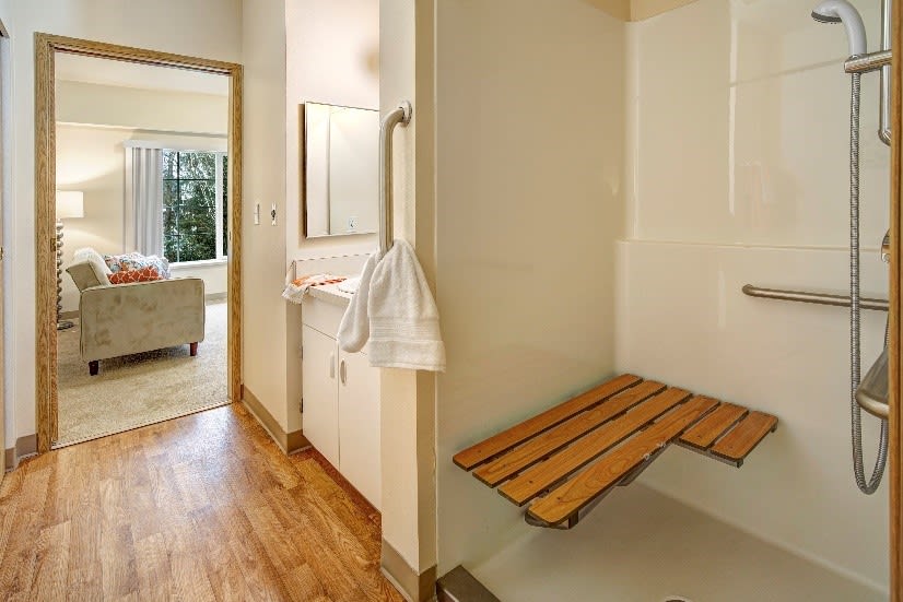 Accessible bathroom with a wooden bench and grab bar in the shower area.