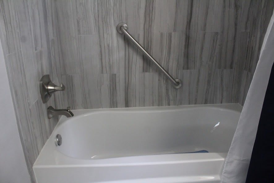 A modern bathtub with a grab bar and tiled wall.