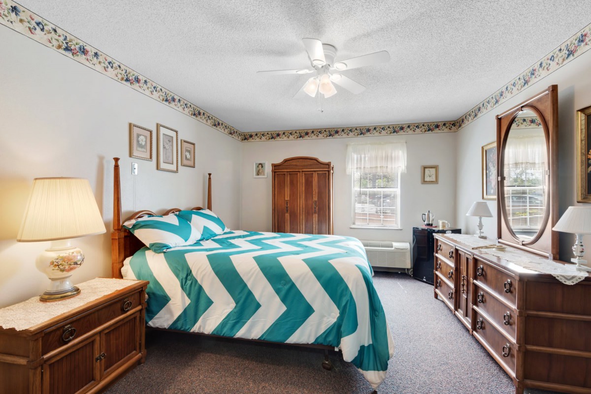 A cozy bedroom with a teal and white chevron-patterned bedspread, wooden furniture, and decorative elements.