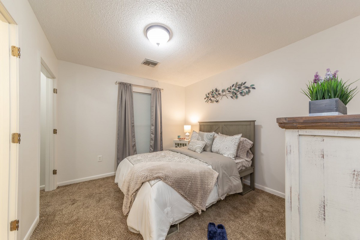 A cozy bedroom with a neatly made bed, bedside lamp, and simple decor.