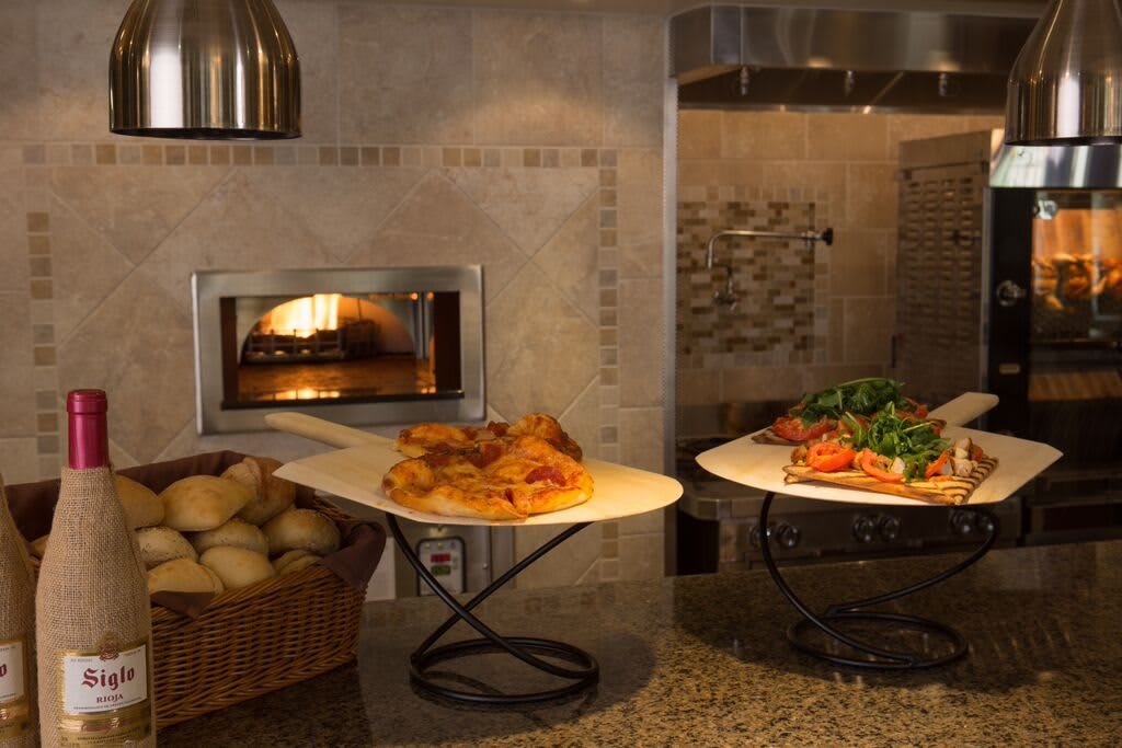 A cozy kitchen scene featuring freshly baked pizza and bread by a stone oven.
