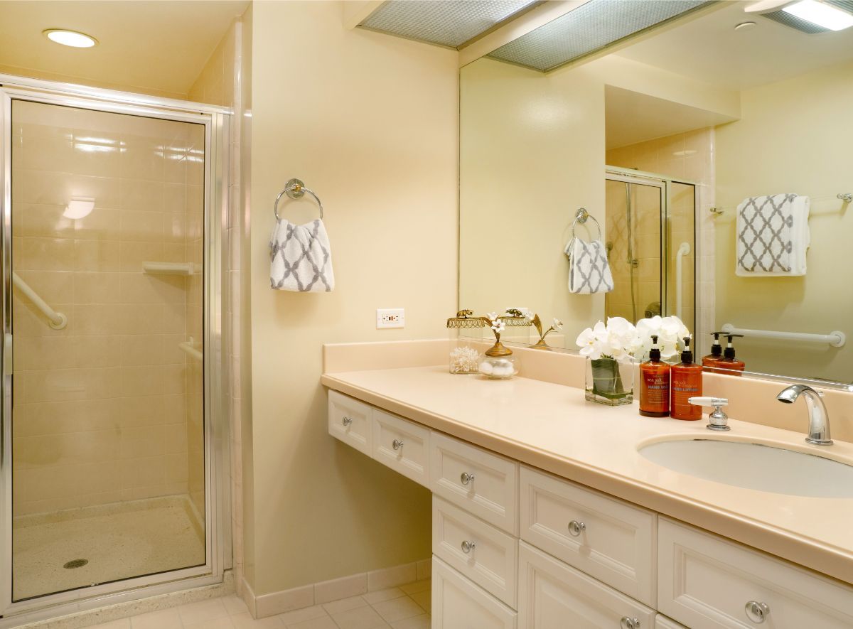 A well-lit bathroom with a shower, sink, and mirror.