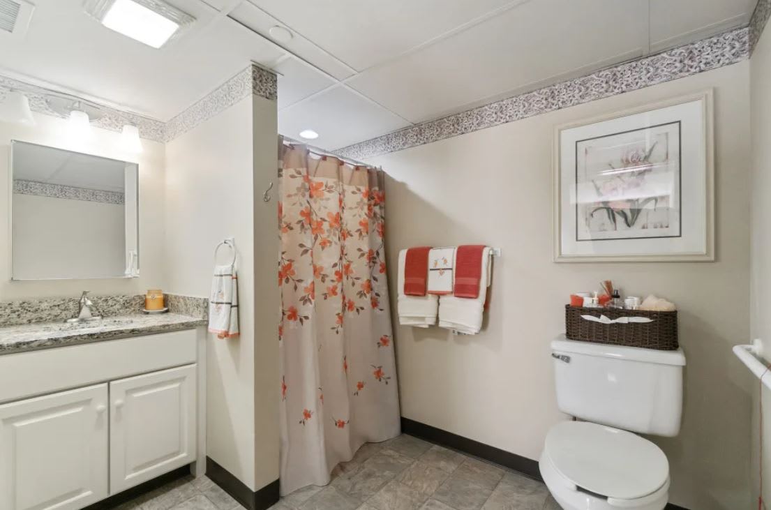 A well-organized bathroom featuring a shower with a floral curtain, a sink, neatly arranged towels, and decorative elements.