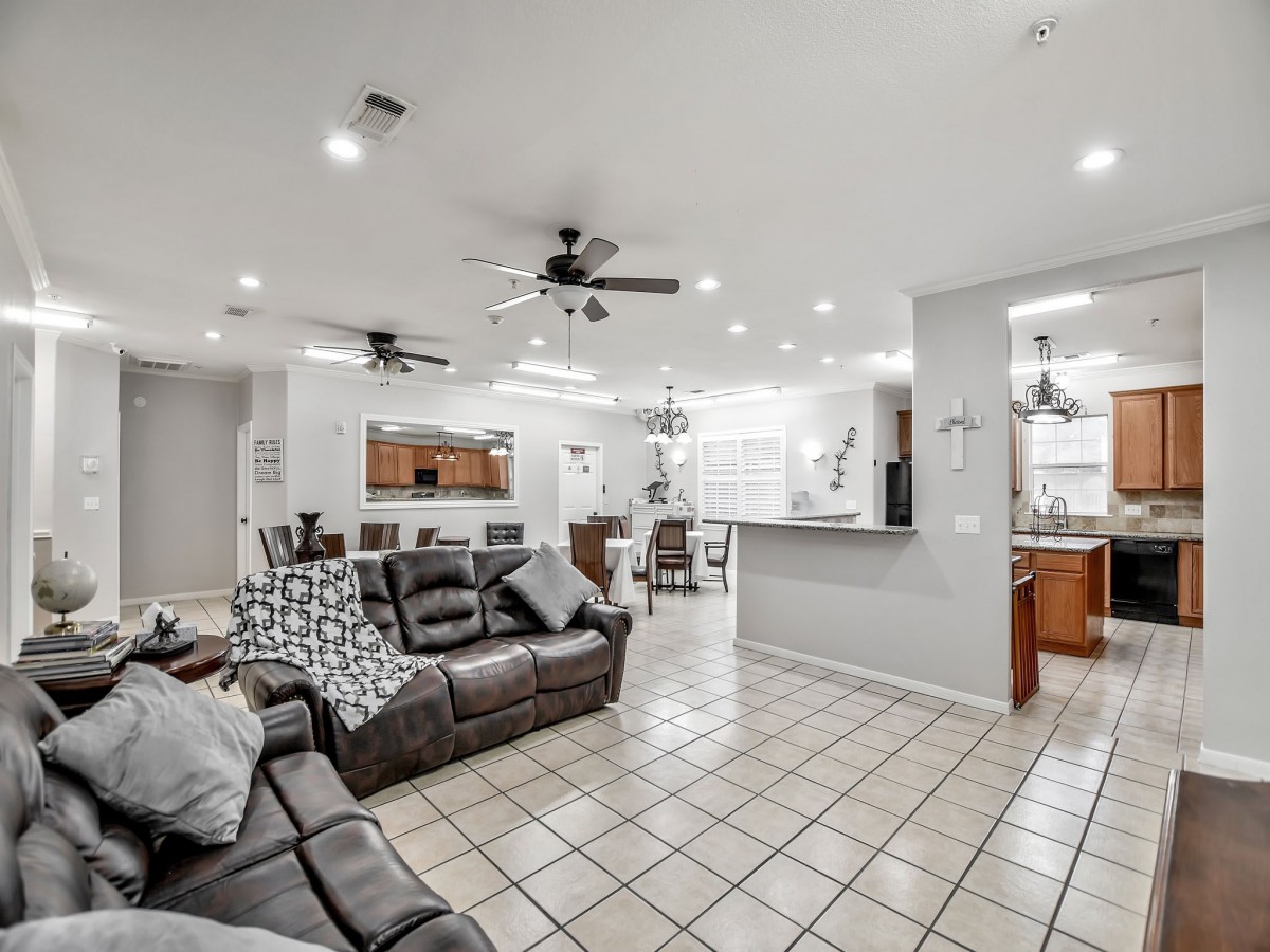 A modern open-space living room with a view into the kitchen, featuring comfortable furniture and tile flooring.