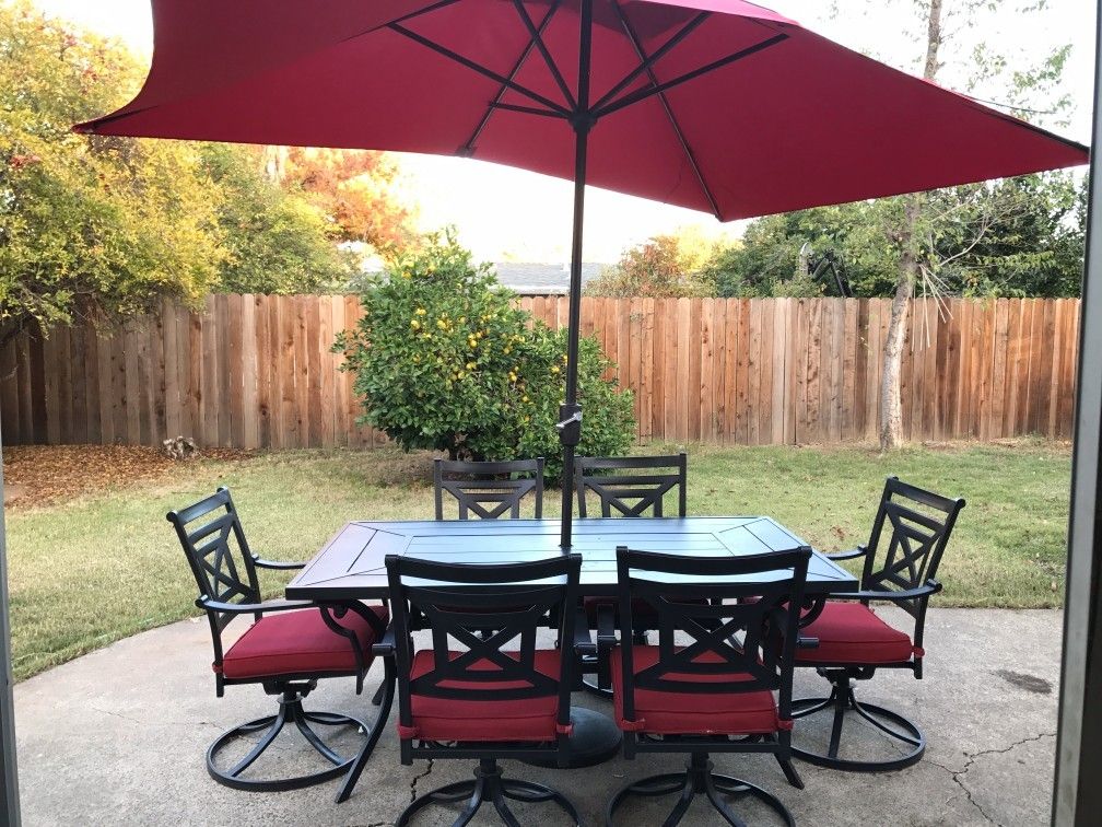 A patio set with a red umbrella and chairs in a backyard.
