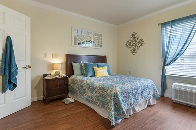 A cozy bedroom with a double bed featuring a colorful quilt, a wooden nightstand with a lamp, and decorative wall art.