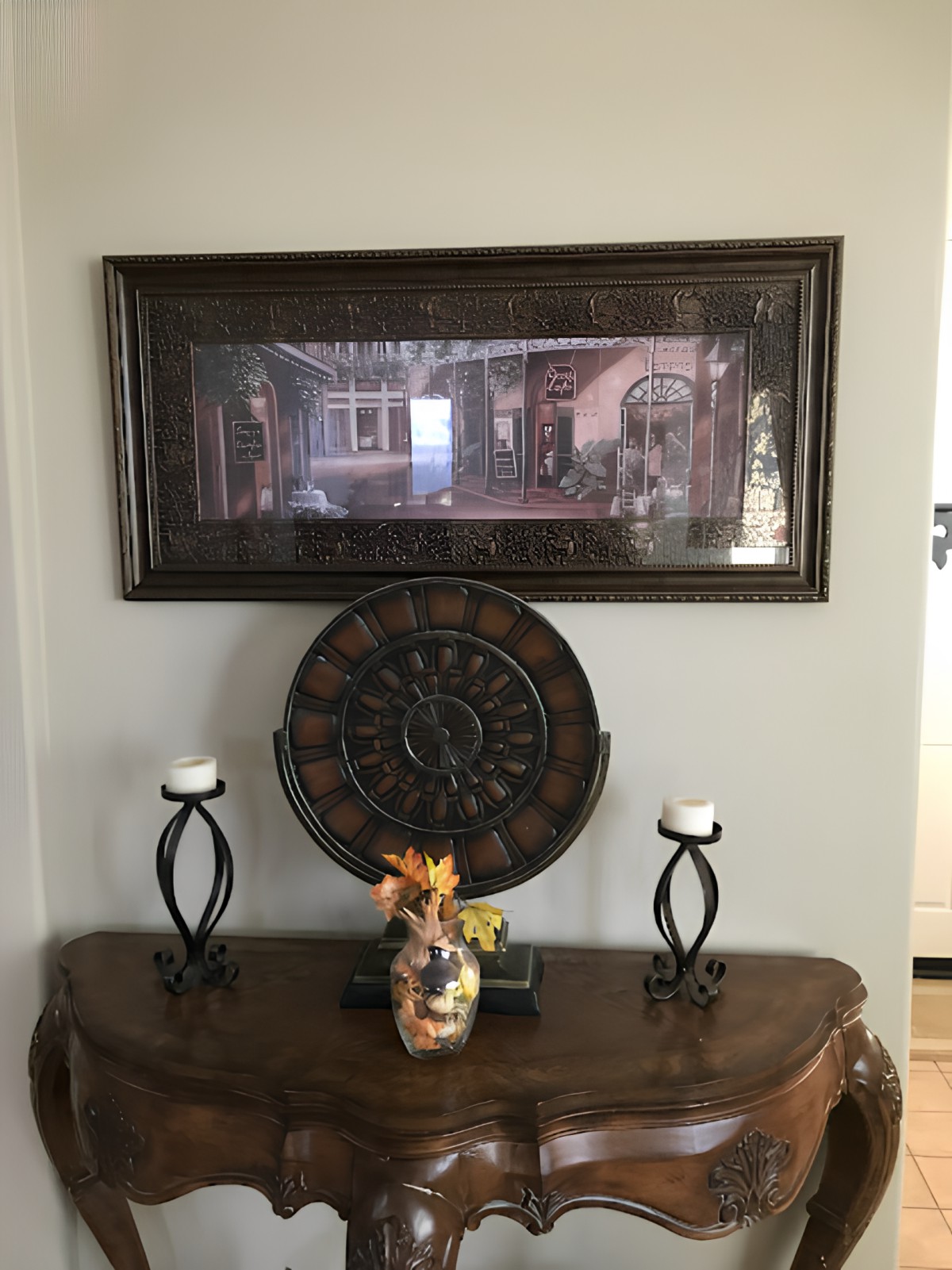 A tastefully decorated interior space featuring a framed picture, decorative wall clock, and a table adorned with candle holders and a vase of flowers.