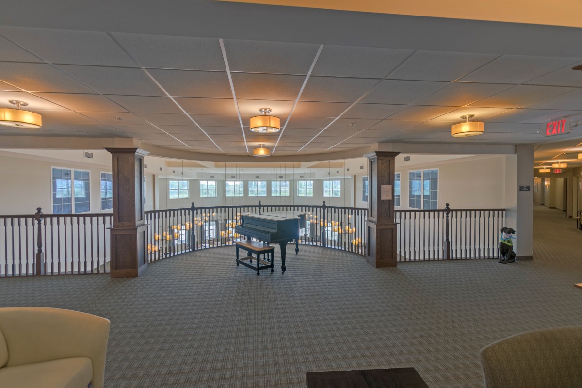 A spacious interior with a piano on a carpeted floor, surrounded by windows and banisters.