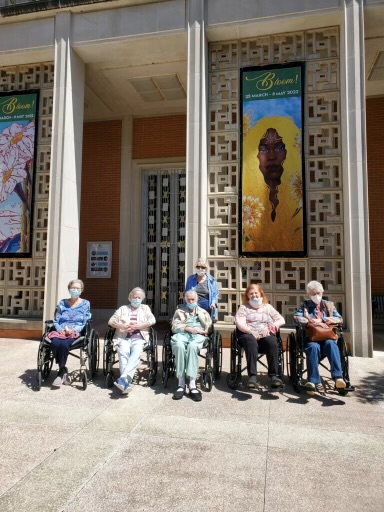 A group of elderly individuals enjoying a sunny day in front of colorful murals.