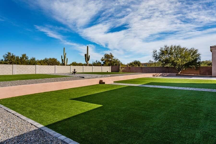 A landscaped backyard with artificial grass, desert plants, and clear blue skies.