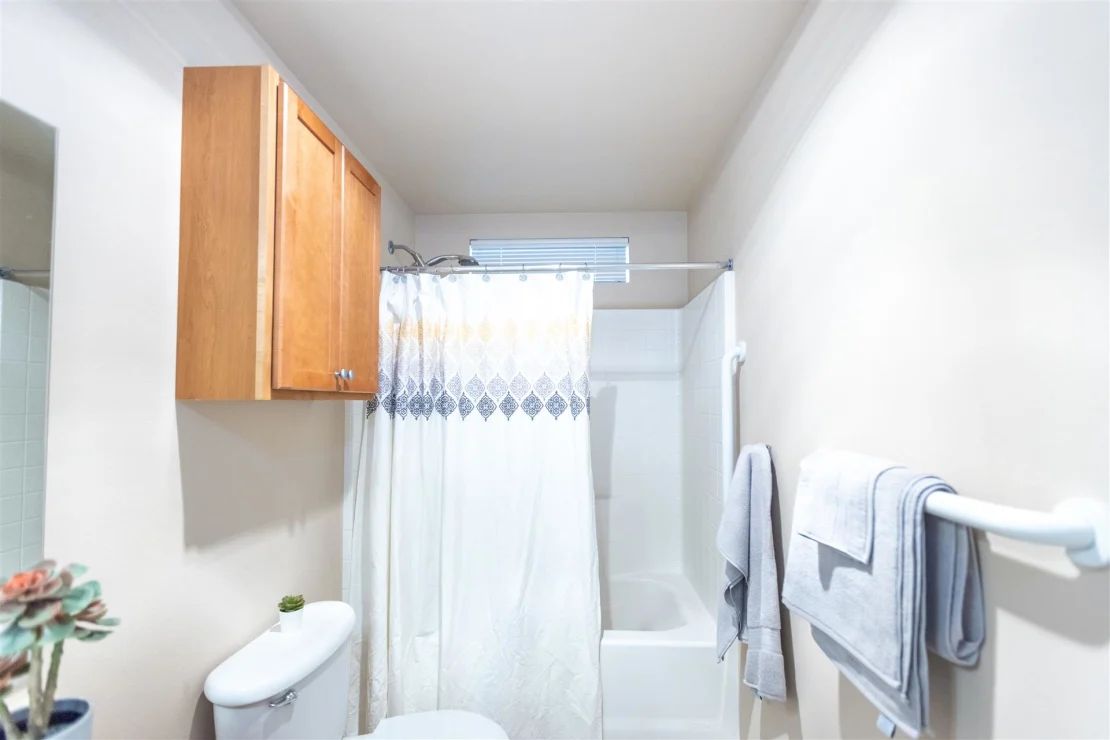 A compact and neatly organized bathroom with a shower and wooden cabinet.