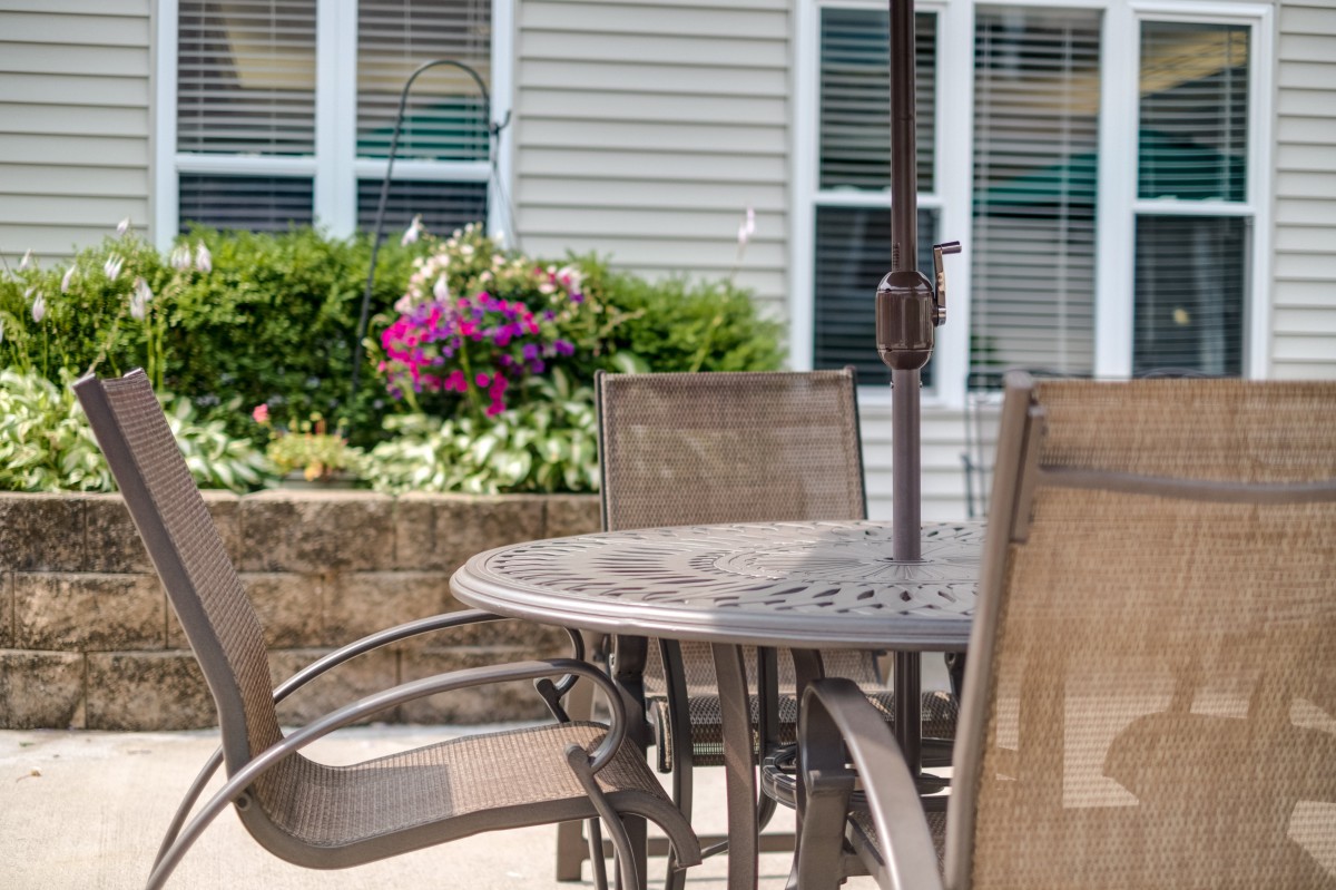 A sunny patio setup with a table and chairs, surrounded by a garden with blooming flowers.