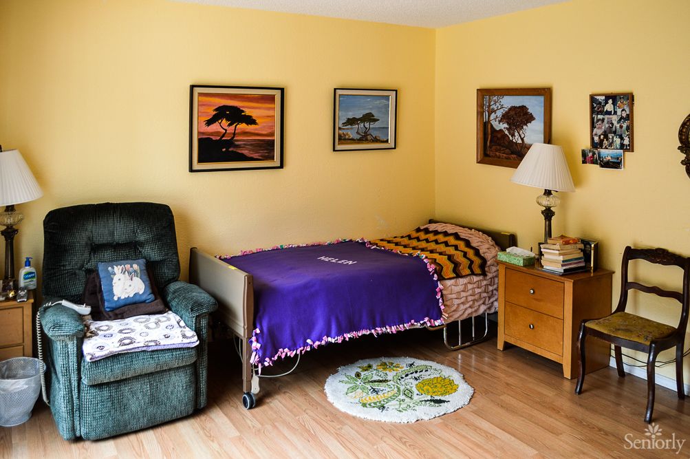 A cozy bedroom featuring a single bed with a colorful blanket, an armchair, and wall art.