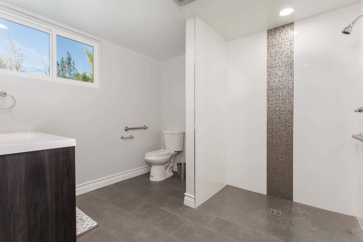 A modern and minimalist bathroom featuring a toilet and open shower area with tile flooring.