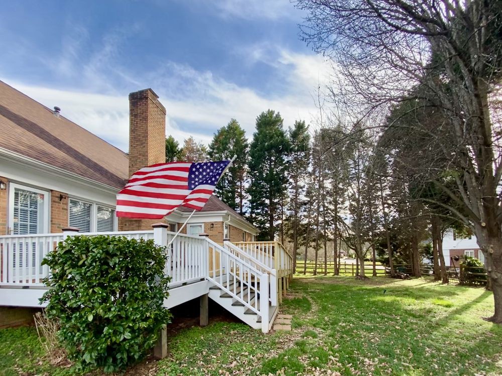A backyard view with an American flag on a deck, surrounded by trees and grass.