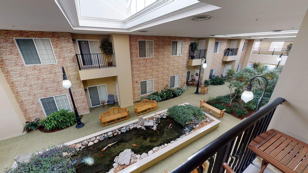 A view of an indoor courtyard with a skylight, featuring plants, a small pond, and seating areas.
