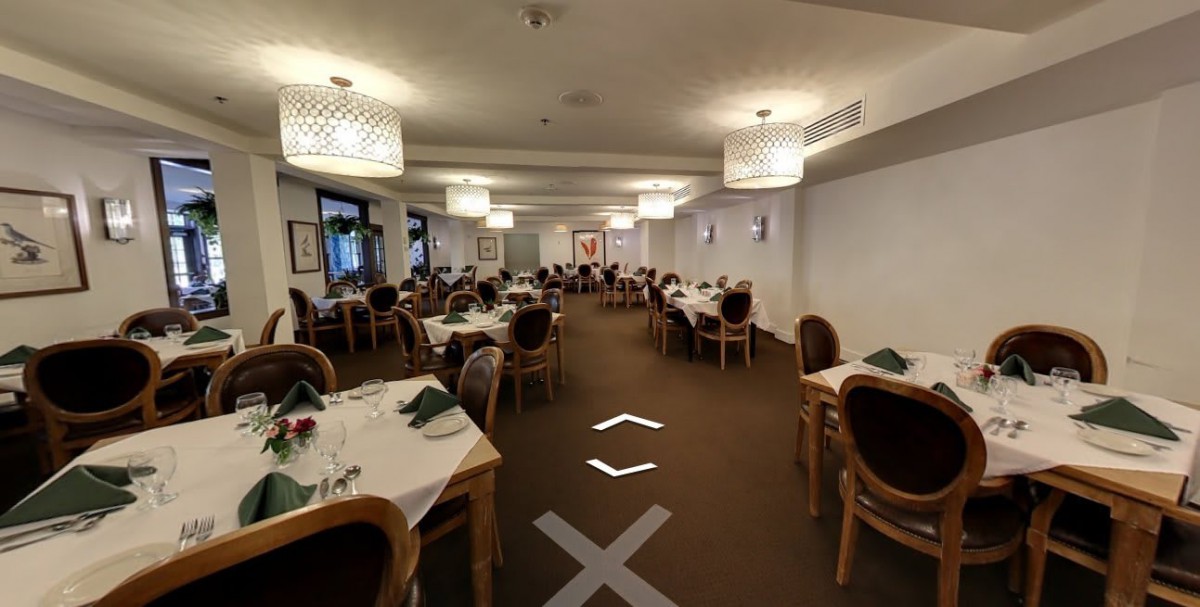 A spacious restaurant dining area with neatly arranged tables and chairs, well-lit by modern hanging lights.